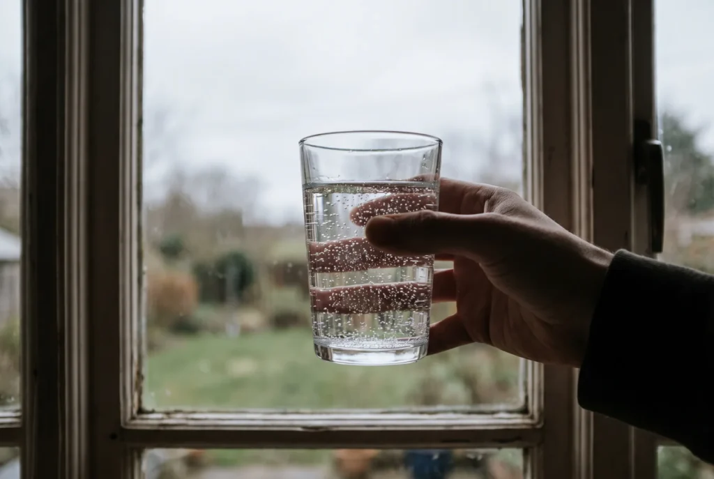 Glass of well water full of tiny bubbles held up to a kitchen window