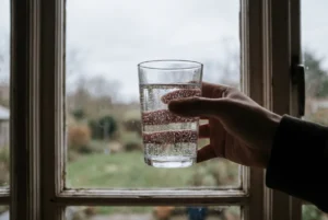 Glass of well water full of tiny bubbles held up to a kitchen window